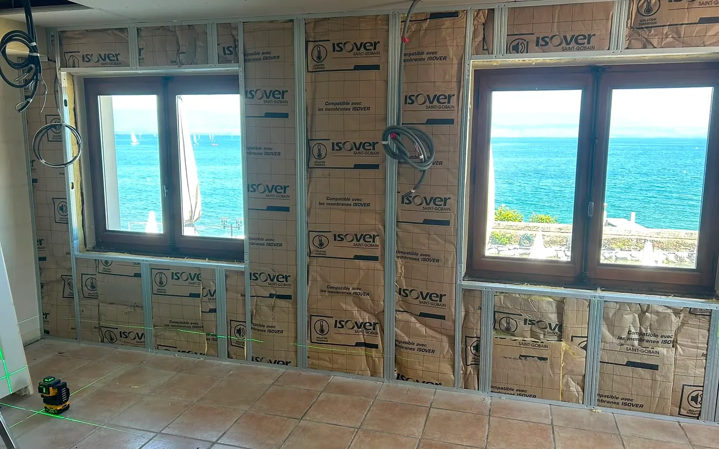 Pièce en chantier face au lac Léman, murs isolés et niveau laser vert au sol